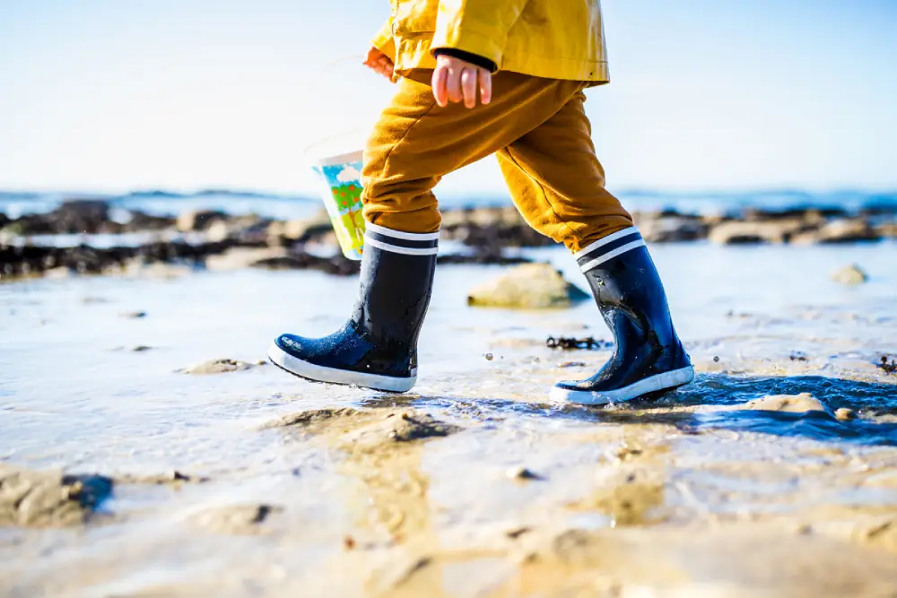 gros plan sur les jambes d'un enfant, en bottes bleues et blanches, pantalon et ciré jaune, sur la plage près de Saint-Brieuc.