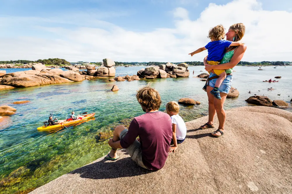 Trégastel, à 15 minutes du centre-ville de Lannion. Une famille sur un rocher, père, mère et deux enfants regardent la mer avec un kayak qui passe.