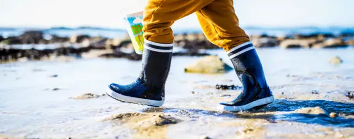 gros plan sur les jambes d'un enfant, en bottes bleues et blanches, pantalon et ciré jaune, sur la plage près de Saint-Brieuc.